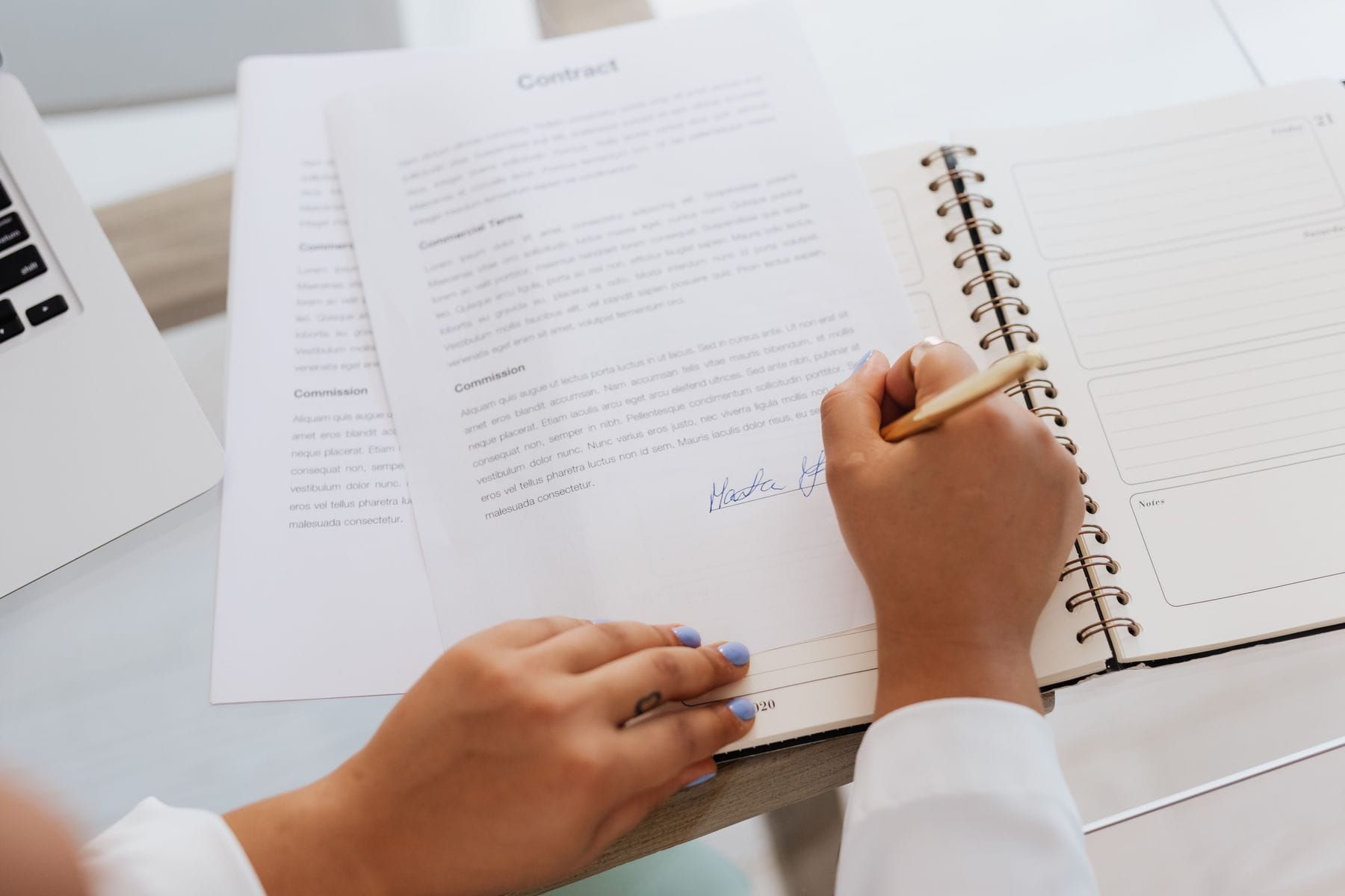 Hands signing a business contract on a desk with office supplies