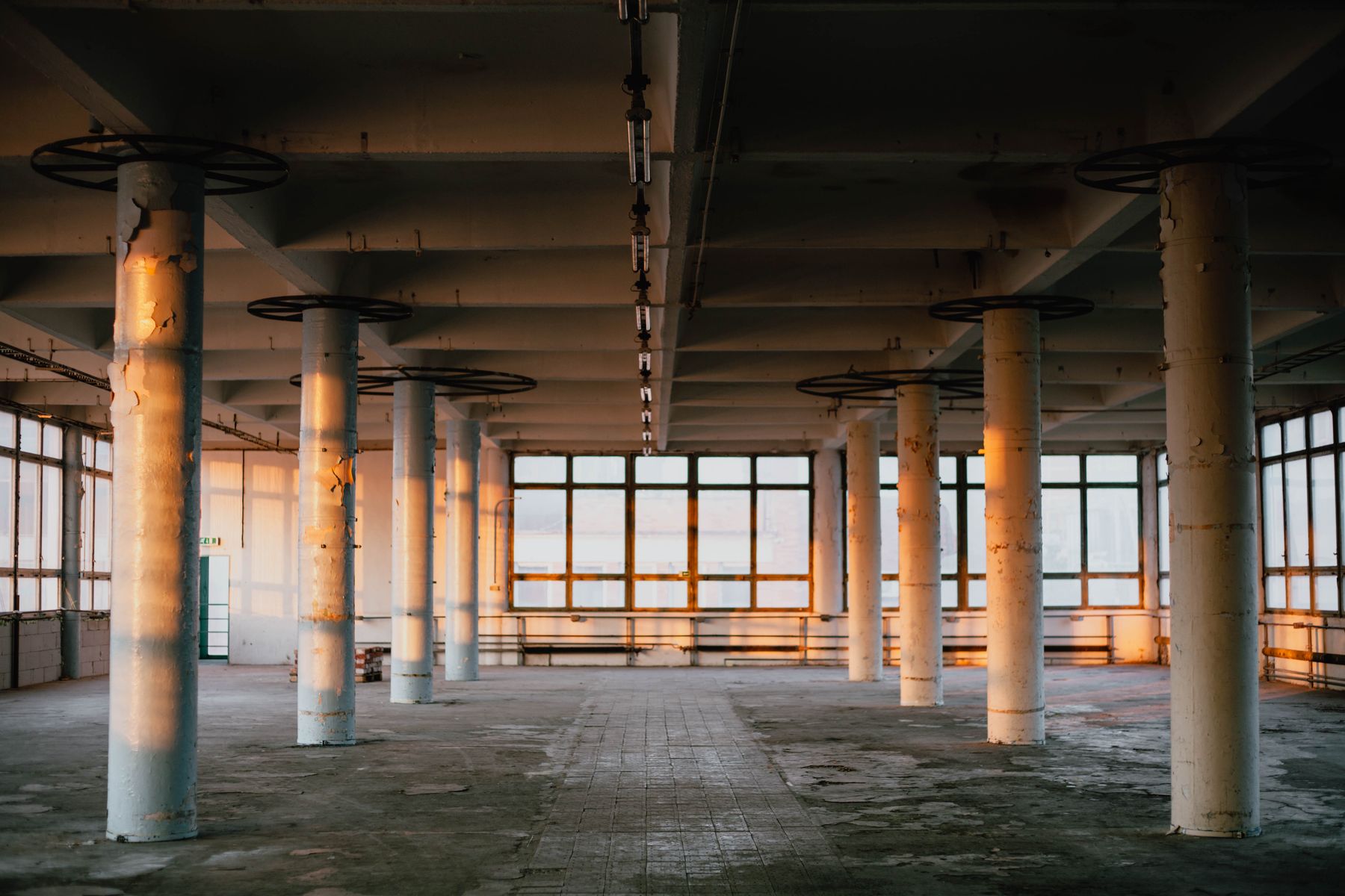 Empty industrial hall with concrete columns lit by daylight through tall windows